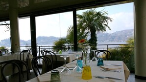 Un restaurant dont les tables sont dressées pour le service, avec vue sur un lac et des collines en arrière-plan.