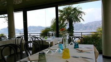 A restaurant with tables set for dining, overlooking a lake with hills in the background.