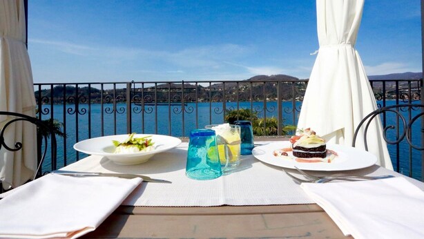 Une table sur un balcon avec vue sur la mer, deux assiettes de nourriture et deux verres d’eau.