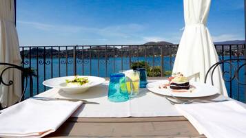 A balcony table with a view of the sea, two plates of food, and two glasses of water.