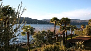Une vue sur le lac, avec des palmiers, une terrasse en bois et une chaîne de montagnes à l’horizon.
