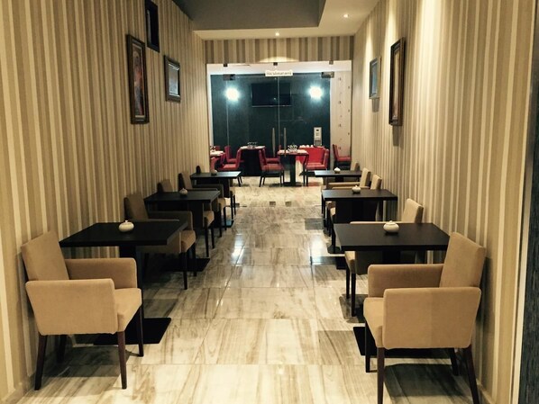 Un restaurante con papel tapiz a rayas, suelo de mármol y sillas rojas y beige.