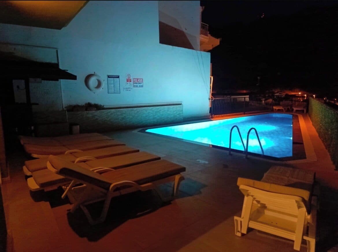 A pool area with lounge chairs, a sign indicating a poolside area, and a building in the background.