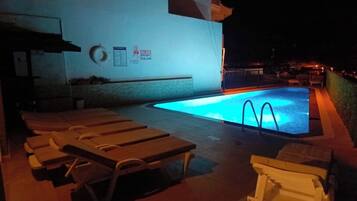 A pool area with lounge chairs, a sign indicating a poolside area, and a building in the background.