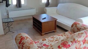 A living room with a white sofa, a floral-patterned sofa, a wooden coffee table, a TV on a stand, and a window with curtains. - Es Apartments (Marmaris)