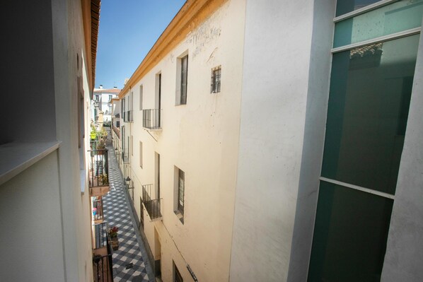 Une ruelle étroite entre deux immeubles dotés de balcons, un sol à carreaux et un ciel dégagé.