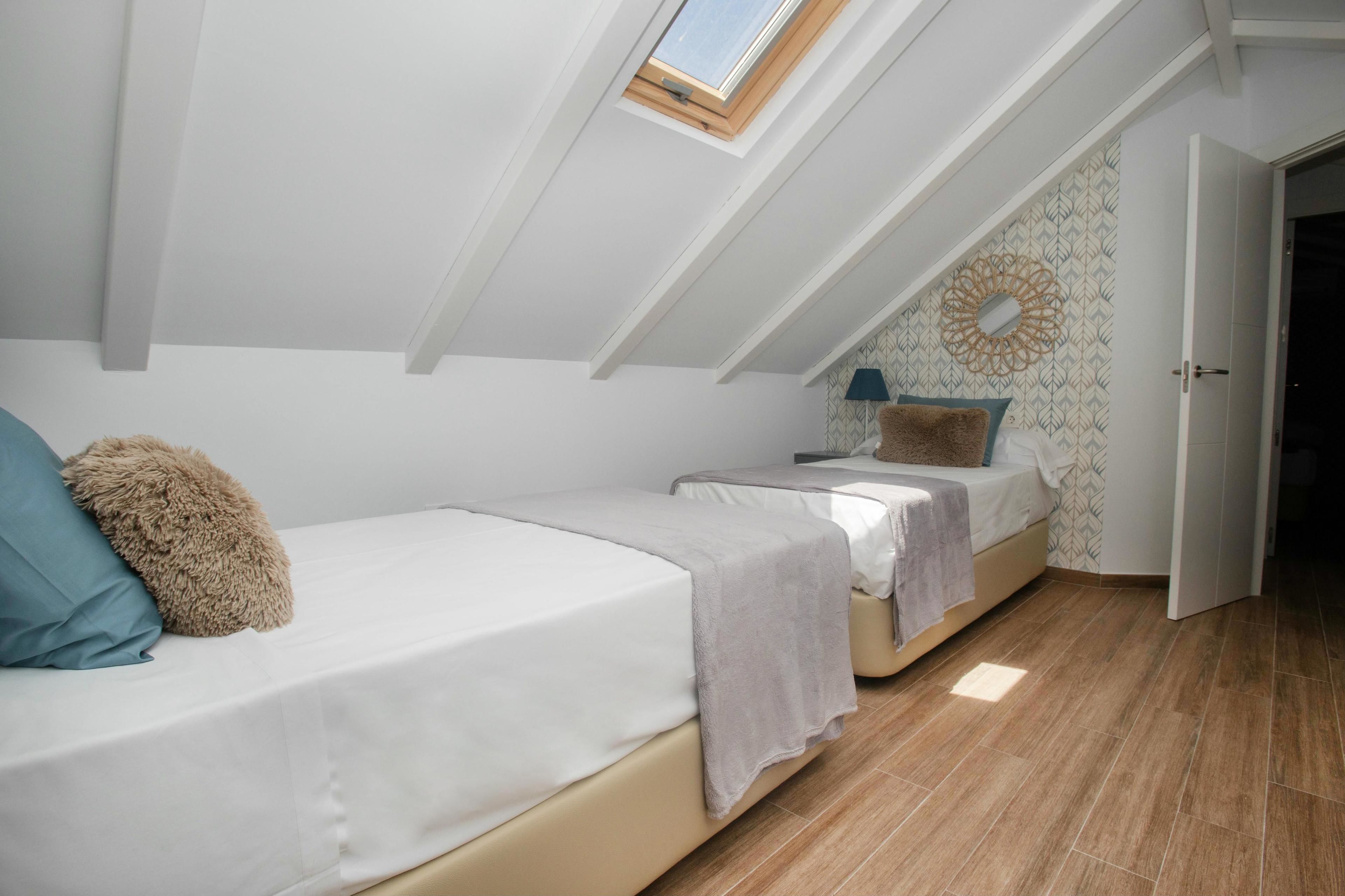 A bedroom with two beds, a skylight, patterned wallpaper, and a door leading to another room.