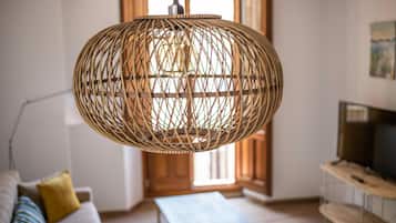 Een kamer met een wilgentak hanglamp, een bank met kussens, een televisie op een houten standaard en een houten vloer.