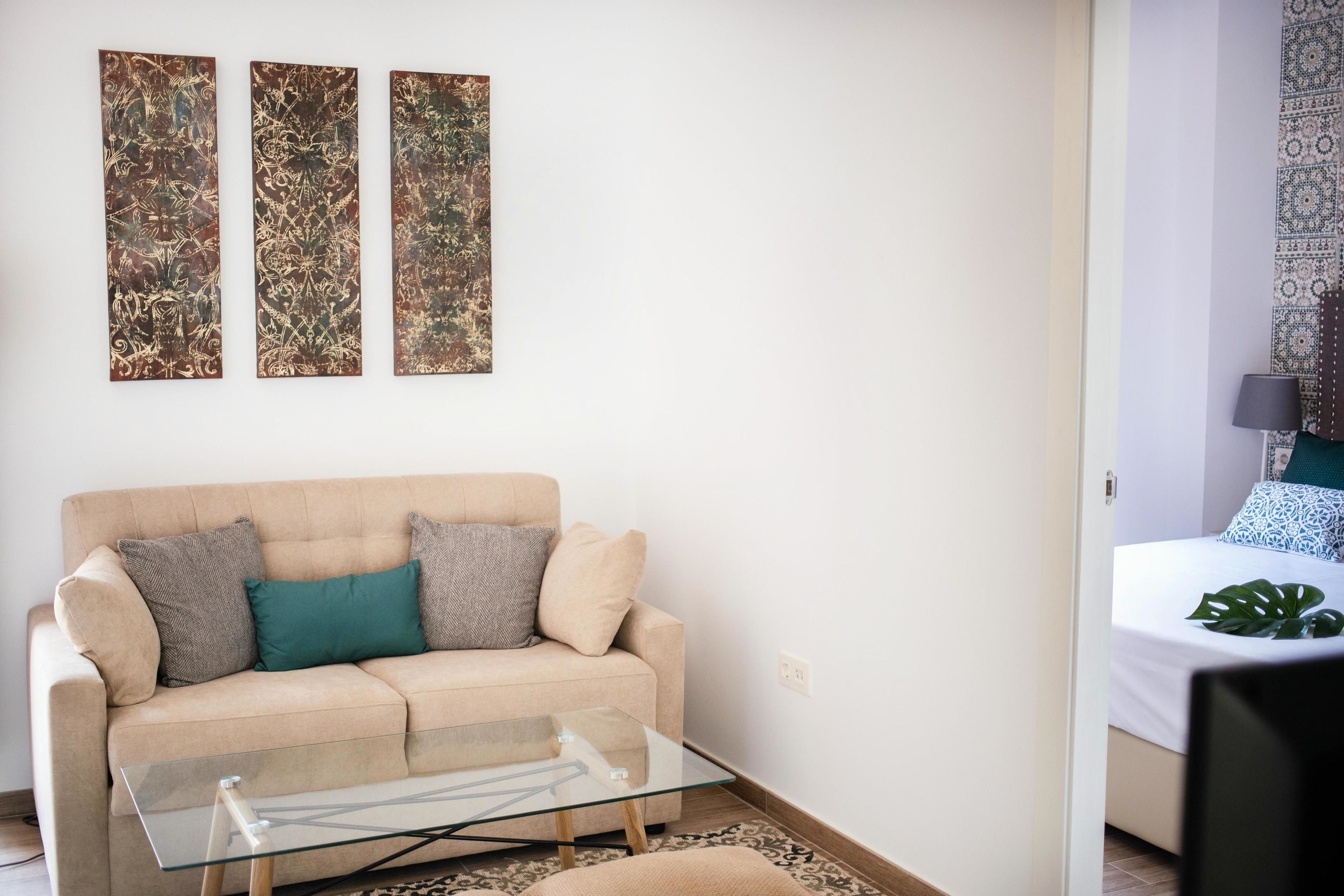 Een moderne woonkamer met een beige bank, een glazen salontafel en drie abstracte schilderijen aan de muur.