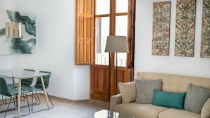A living room with a glass coffee table, a beige sofa with pillows, a dining table with chairs, and artwork on the walls. - Feelathome Mártires Apartments (Málaga)