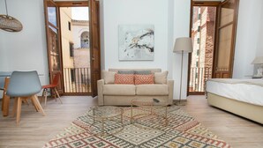 A living room with a beige sofa, a patterned rug, a small coffee table, a chair, and a bed. - Feelathome Mártires Apartments (Málaga)