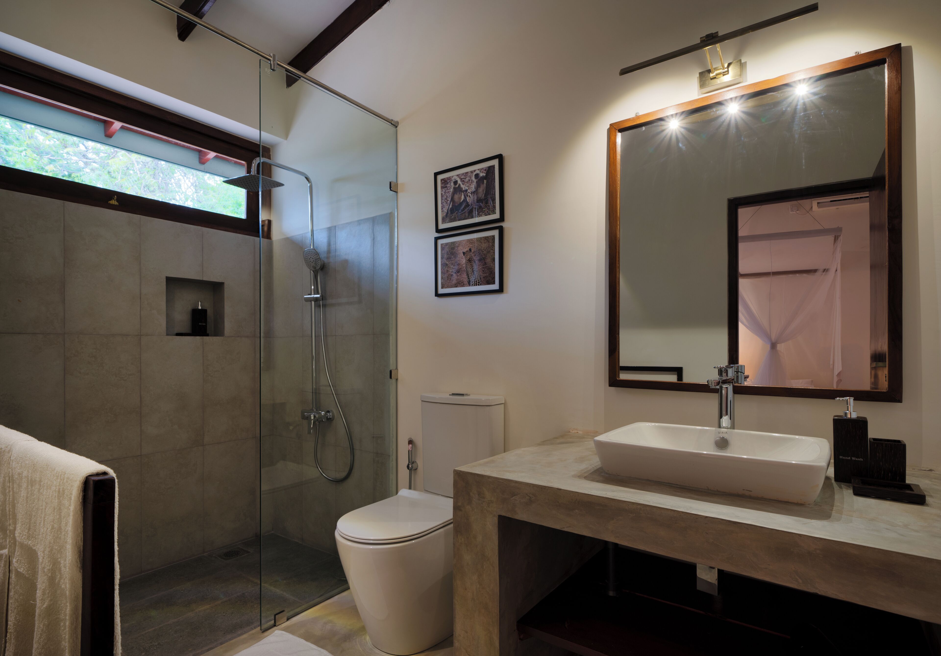 A modern bathroom with a glass-enclosed shower, a white toilet, a large mirror, and a beige vanity.