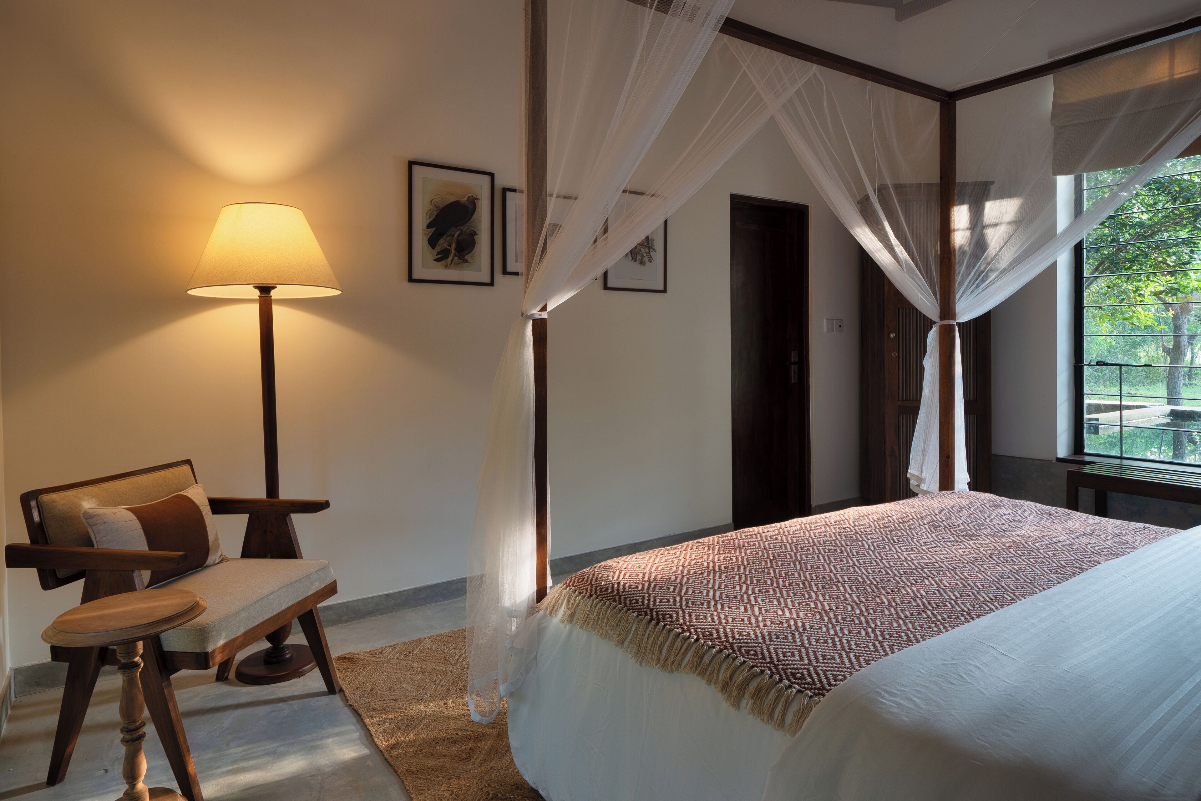 Une chambre à coucher comprenant un lit, une chaise, une table de chevet, une lampe et une fenêtre donnant sur un paysage verdoyant.