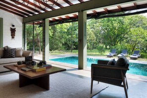 A modern living room with a pool view, a sofa, a coffee table, and a chair. - Neem Tree House (Kirinda)