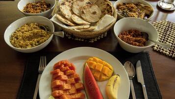 Une table à manger avec divers plats, notamment des galettes, une assiette de mangues, de pastèques et de bâtonnets de carottes, ainsi que des bols contenant différents aliments.