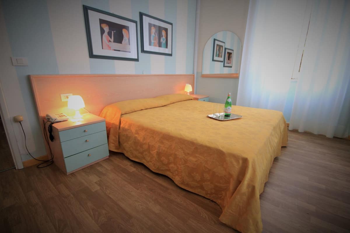 Ein Hotelzimmer mit einem Bett, einem Nachttisch, einer Lampe und gerahmten Bildern an der Wand.