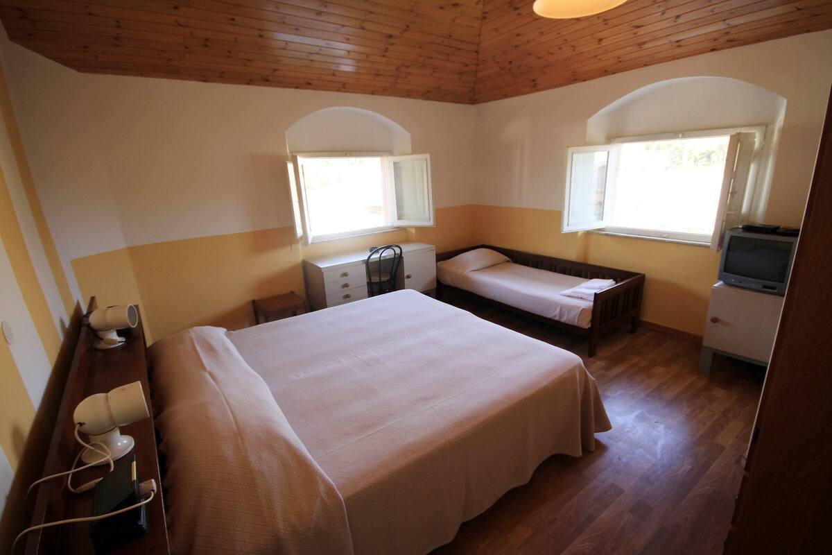 Ein Zimmer mit einem großen Bett, zwei kleineren Betten, einem Fernseher und zwei Fenstern.