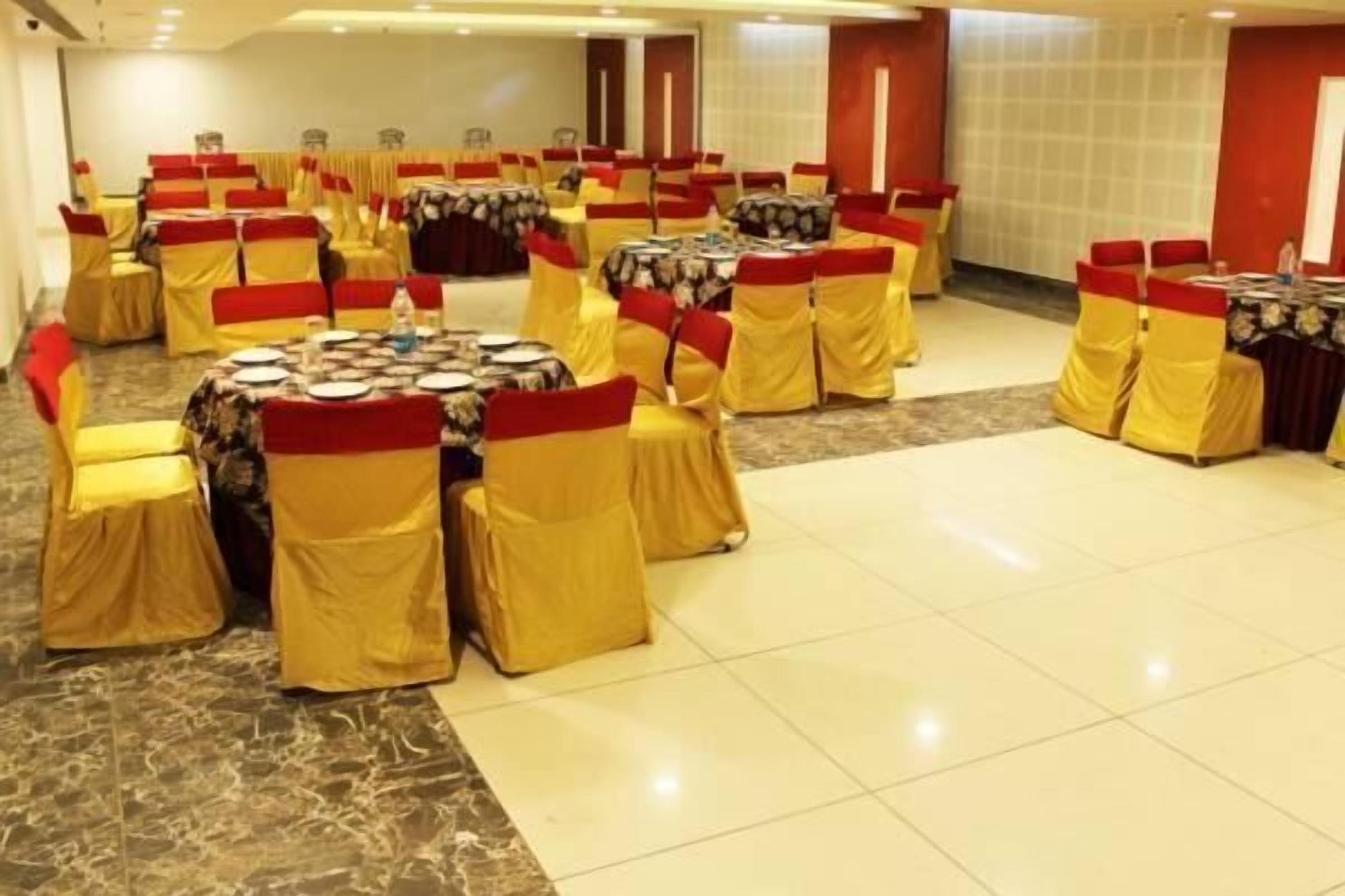 Un salón de banquetes con mesas redondas y sillas, cada una con mantel y cubierta roja y amarilla.