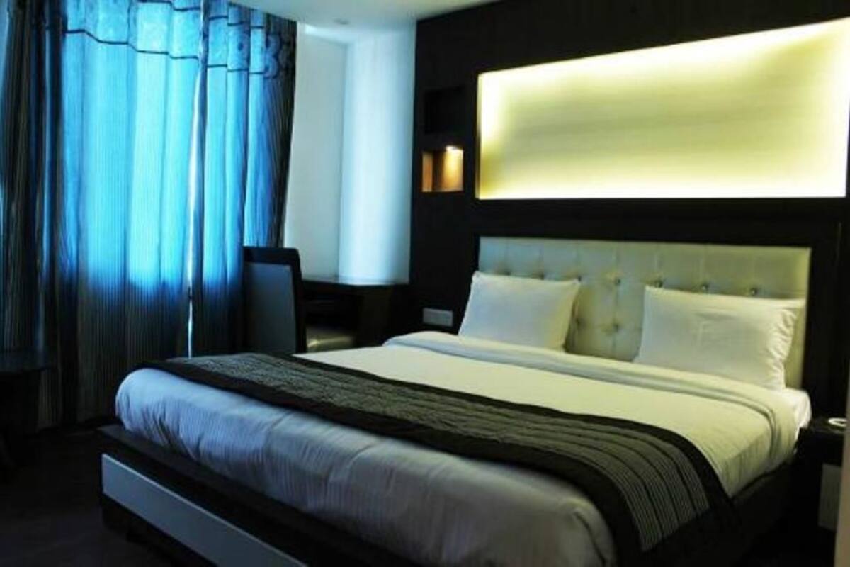 A hotel room with a large bed, a headboard with integrated lighting, a desk, and a chair.