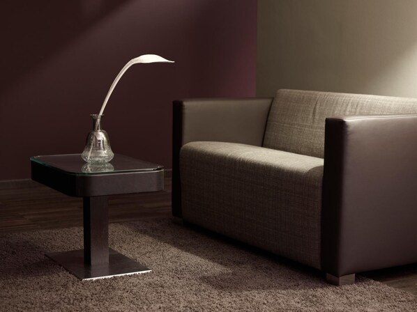 Un salón moderno con un sofá de tonos oscuros y una mesita con un jarrón de cristal y una lámpara metálica.