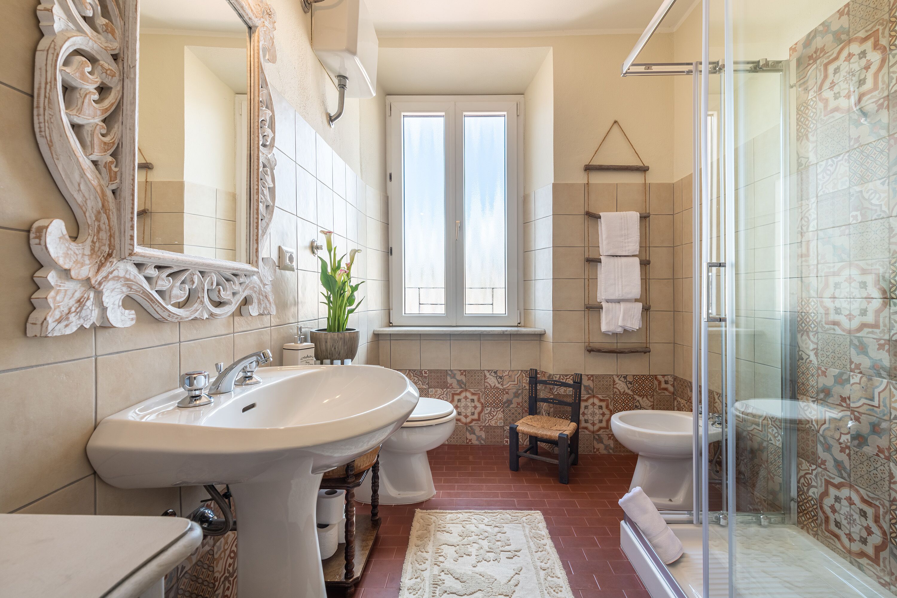 A bathroom with a large mirror, two sinks, a toilet, a shower, and a window.