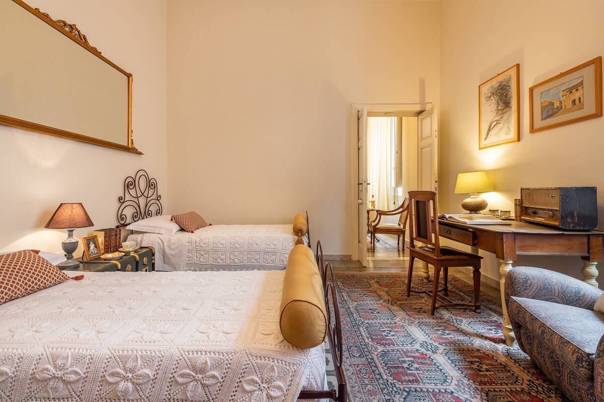 A hotel room with two beds, a desk, a chair, and a patterned rug.