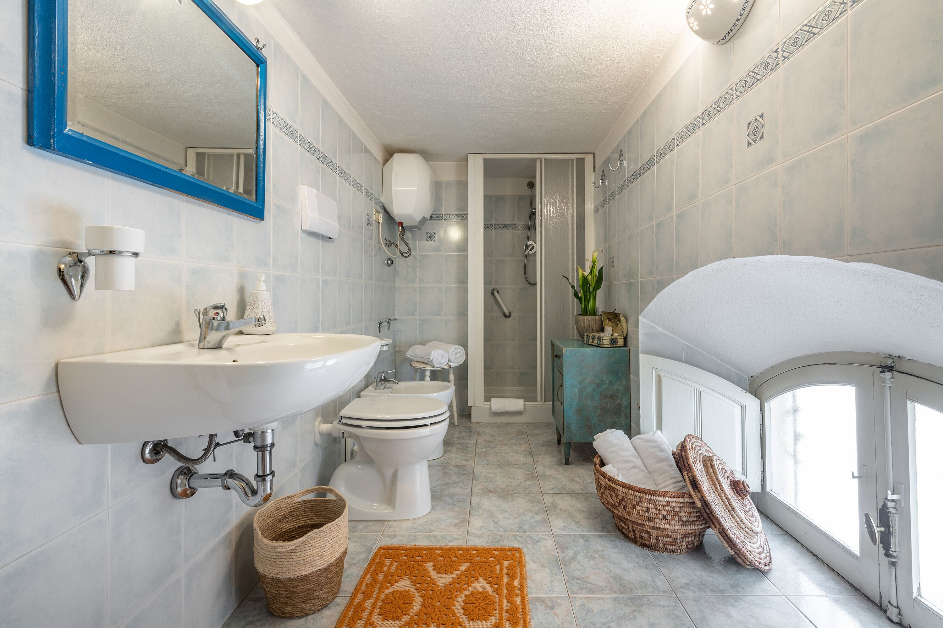 Une salle de bain moderne avec un grand lavabo, des toilettes et une douche. On y trouve des paniers en osier et un tapis décoratif sur le sol.