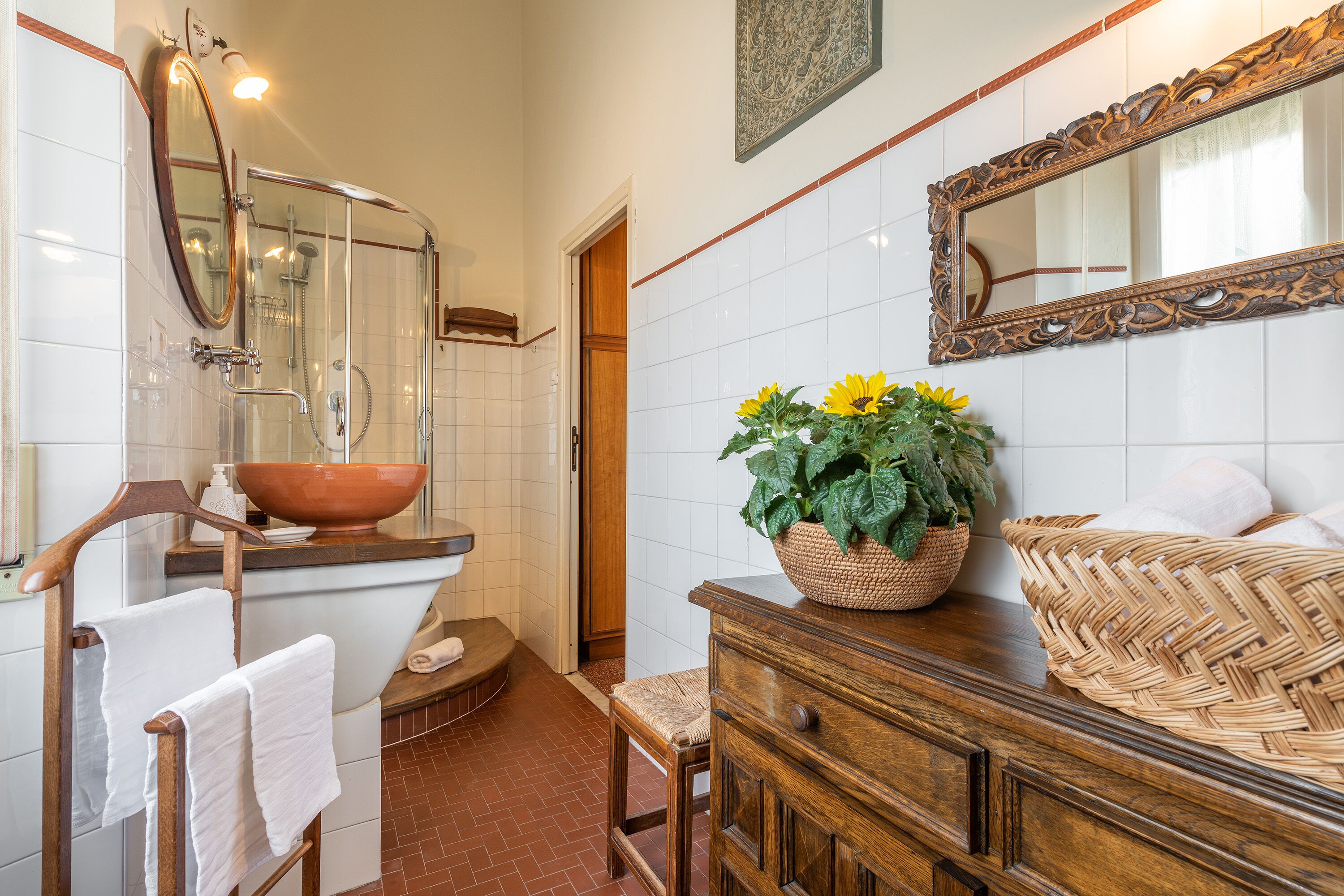 A bathroom with a wooden vanity, a large mirror, a sink with a bowl, and a potted plant.
