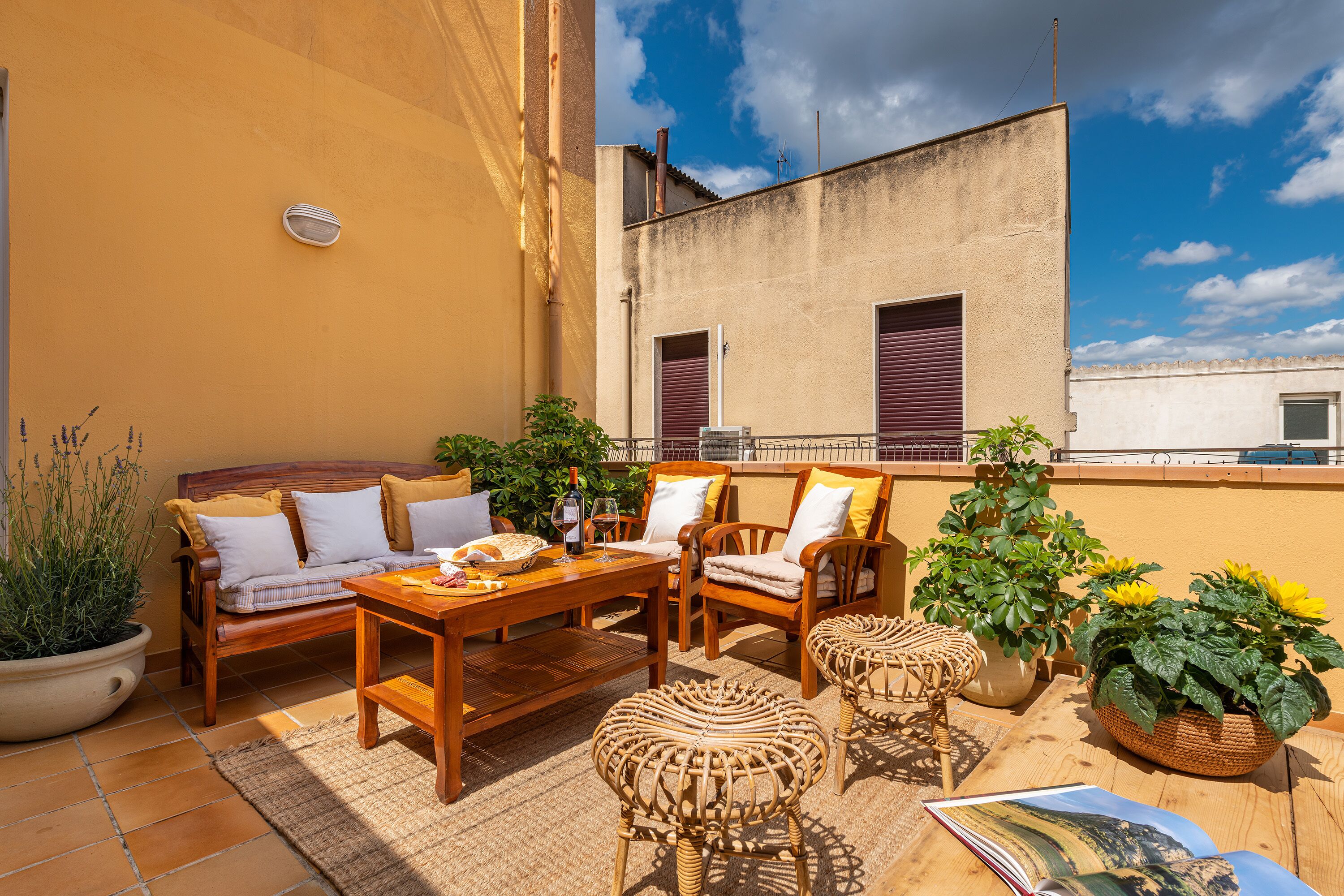 A terrace with a wooden table, wicker chairs, a sofa, and potted plants.