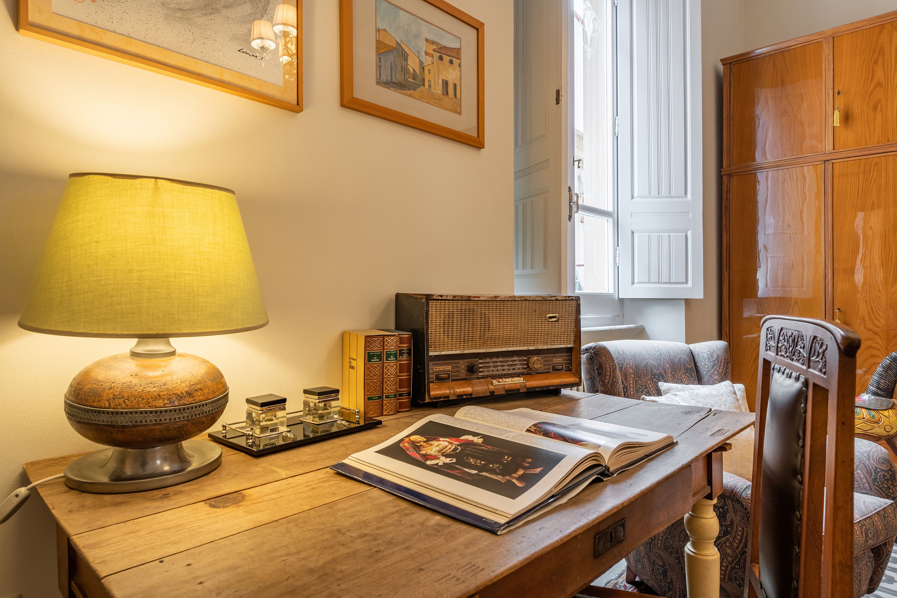 A wooden desk with a lamp, books, a radio, and a chair.