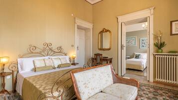 A bedroom with a bed, a sitting area with a chair, a mirror, and a radiator.