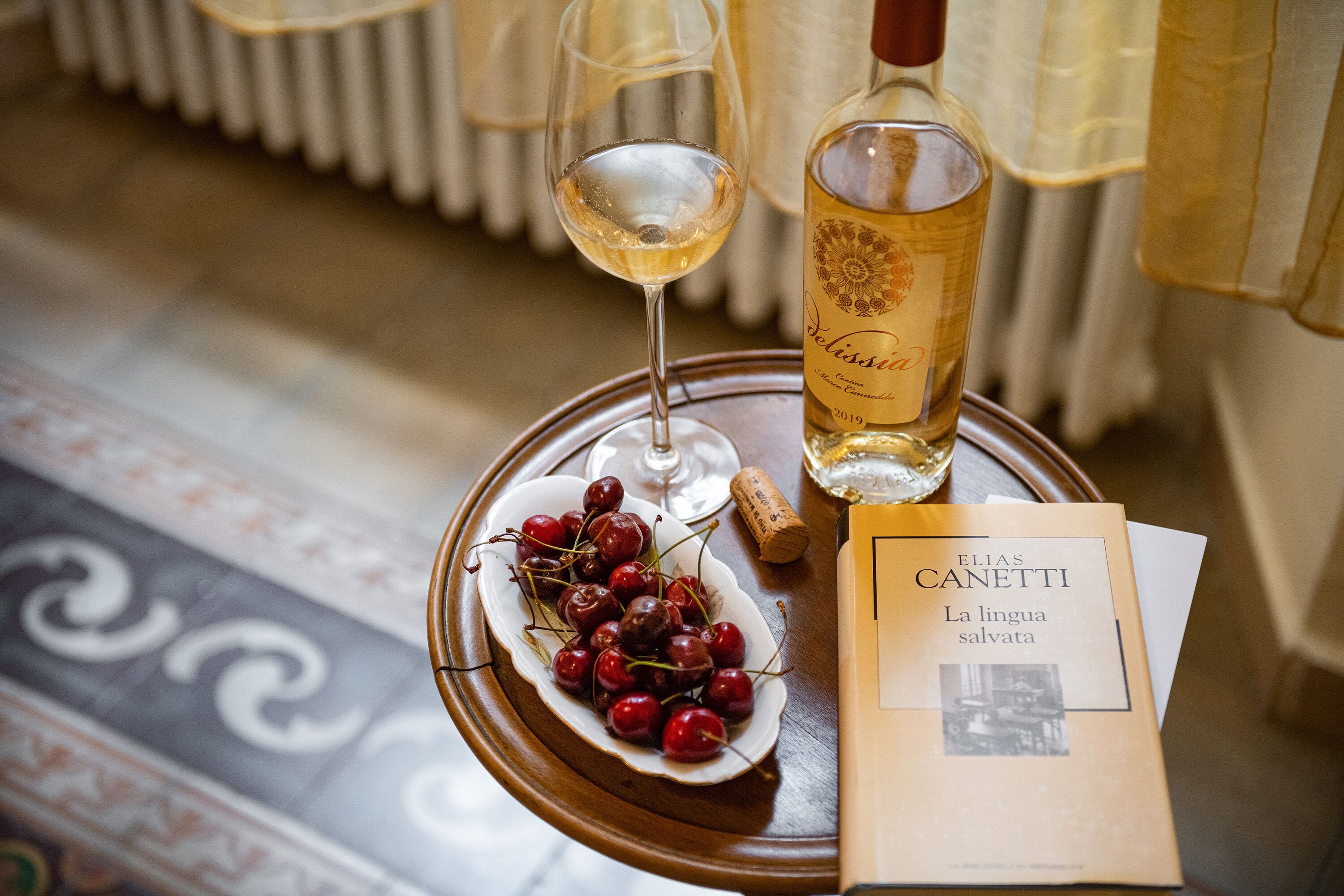 A tray with a bottle of wine, a glass of wine, a plate of cherries, and a book titled "La lingua salvata".