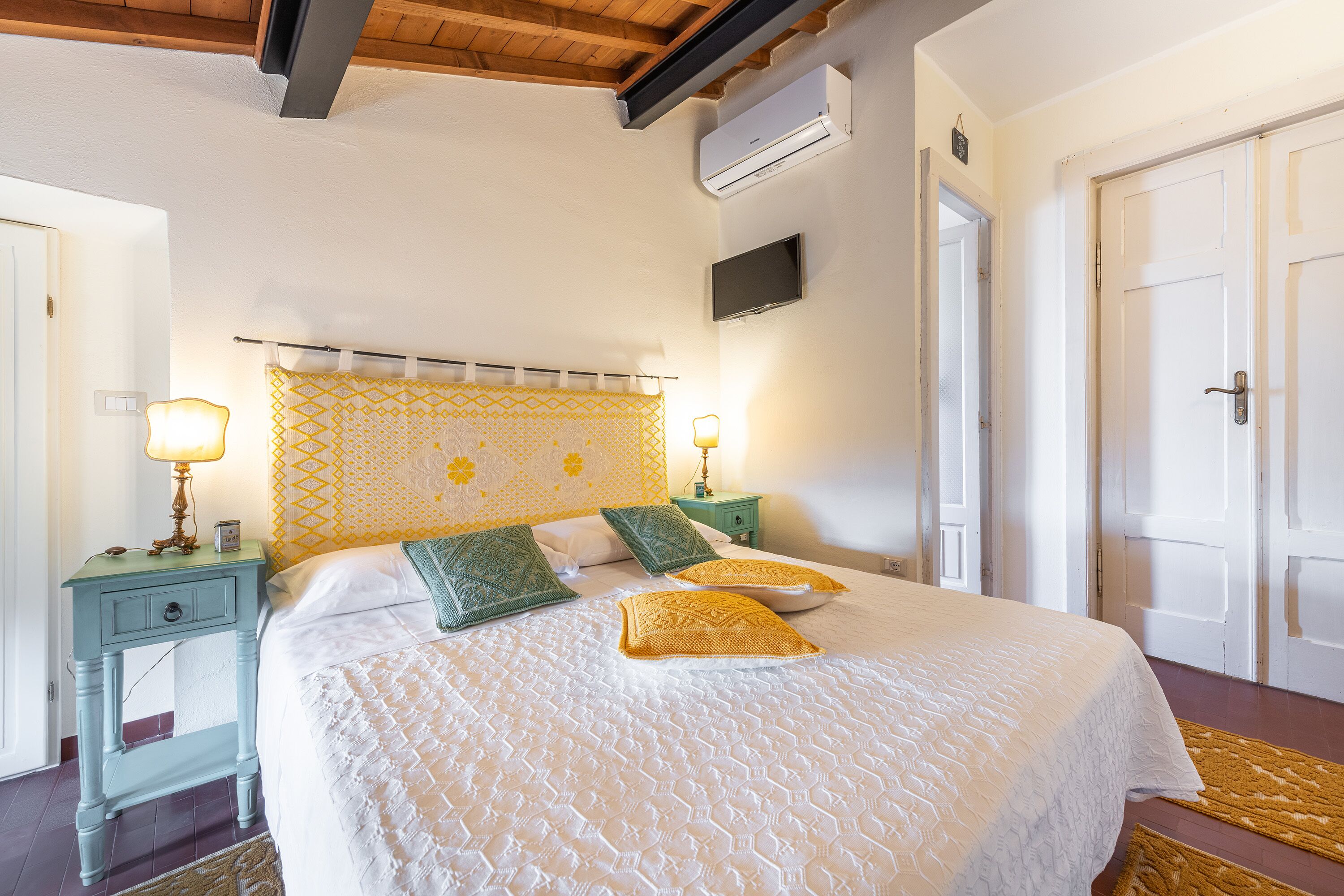 A bedroom with a bed, two nightstands, a wall-mounted TV, and a door.