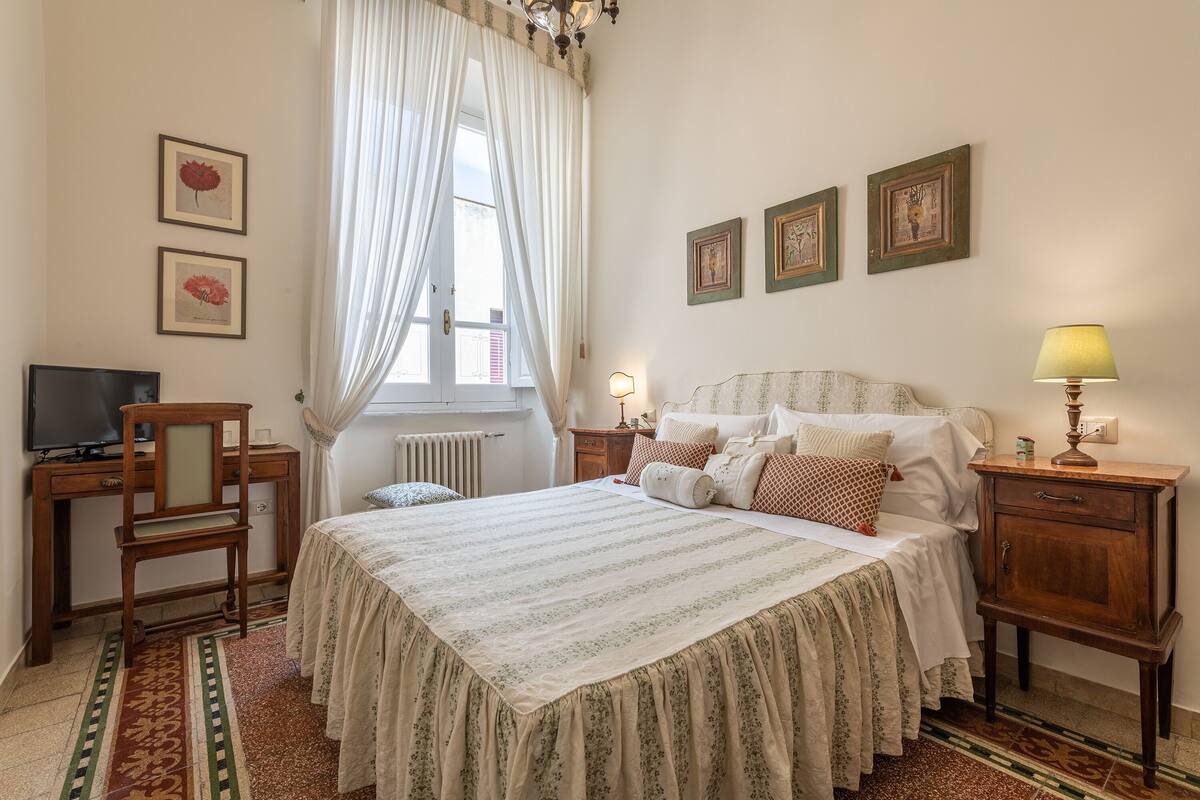 A bedroom with a bed, a desk, a chair, a lamp, and framed pictures on the wall.
