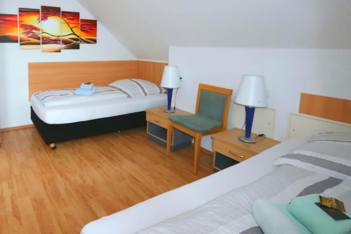 A hotel room with a bed, a desk with a chair, two bedside lamps, a nightstand, and a wall-mounted painting.