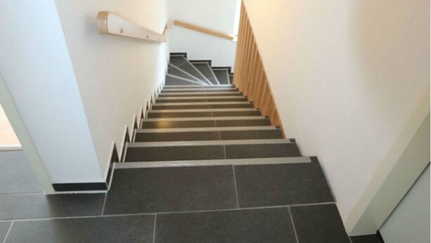 Un escalier moderne, avec un revêtement de sol en carrelage foncé et des rampes en bois, menant à un niveau supérieur.