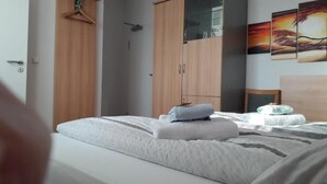 Une chambre à coucher avec un lit, une armoire en bois, un porte-manteau et un tableau accroché au mur.