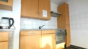 Une cuisine avec des meubles en bois, un four en acier inoxydable et une bouilloire posée sur le plan de travail.