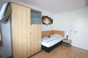 A bedroom with a bed, a wardrobe, a bedside table with a lamp, and a wall-mounted TV. - Penny Pension (Wolfsburg)
