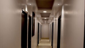 A long, narrow hallway with doors on both sides, leading to individual rooms. The floor is shiny and reflective, and the walls are painted white. - Hotel Maple Inn (Patna)
