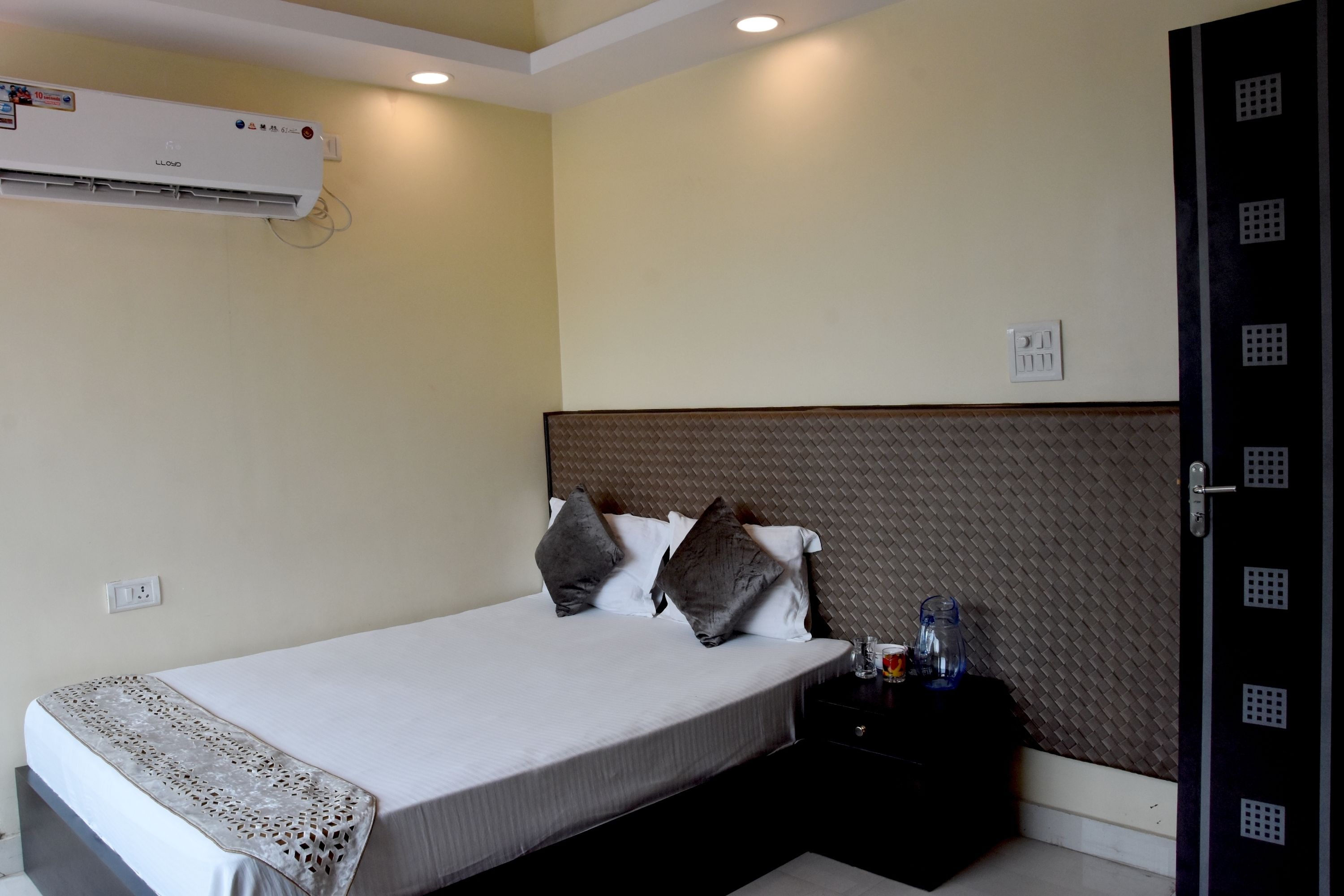 Una habitación de hotel con cama, mesita de noche, dispensador de agua y equipo de aire acondicionado.