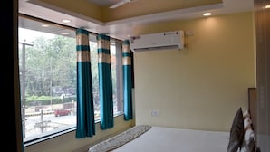 A hotel room with a bed, an air conditioner, a ceiling fan, and a window with curtains. - Hotel Maple Inn (Patna)