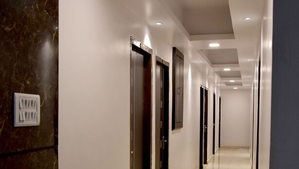 A long, well-lit corridor with a red carpet leading to a series of doors, likely hotel rooms or offices. - Hotel Maple Inn (Patna)
