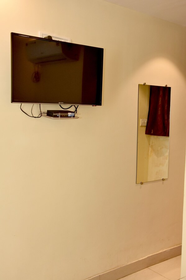 A wall-mounted flat-screen TV and a mirror with a red curtain.