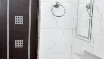 Un baño con pared de mármol blanco, cabina de ducha de vidrio, lavabo blanco y puerta con manija de metal.