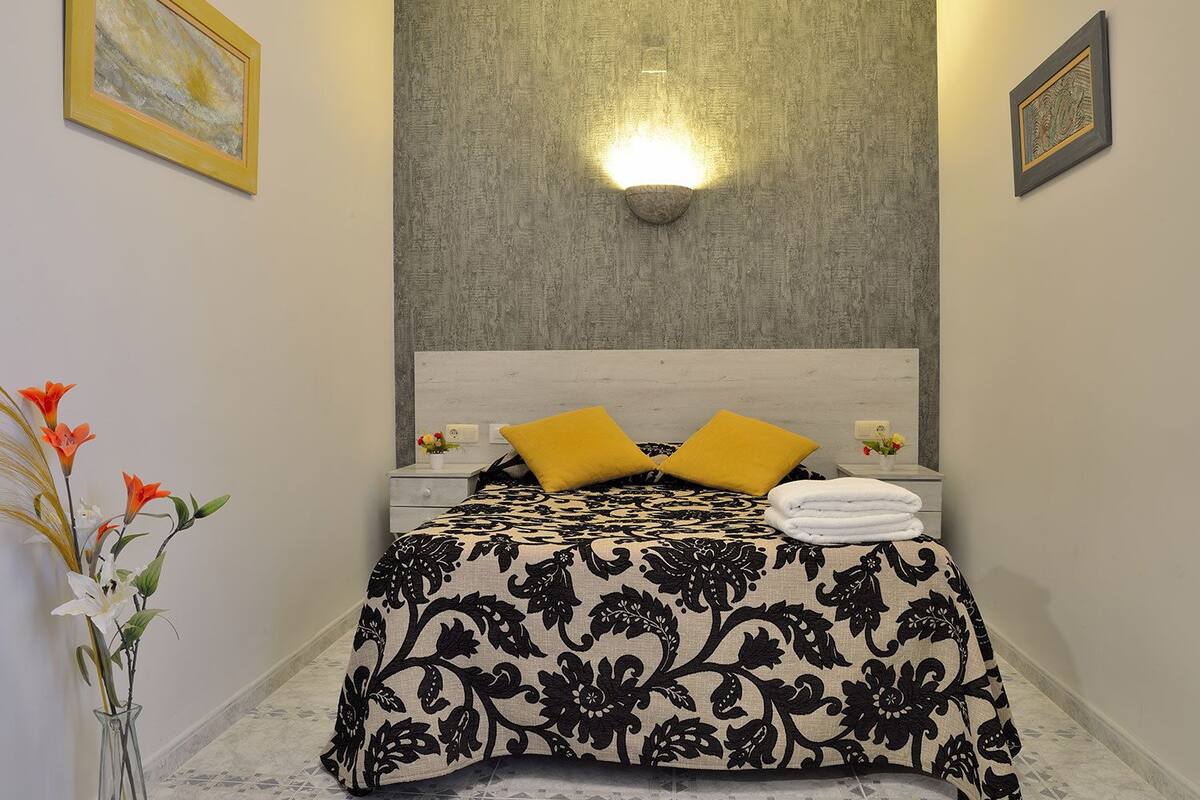 A neatly made bed with a floral bedspread, two yellow pillows, and a white towel on a nightstand.
