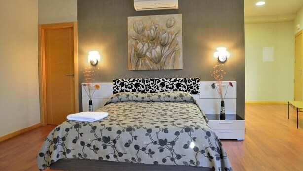 A bedroom with a bed, a wall-mounted air conditioner, and two wall sconces. - Hostal Restaurante Cuatro Caminos (Piedrabuena)