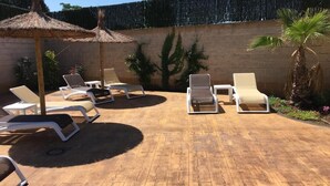 A sunlit patio with lounge chairs and a thatched umbrella, surrounded by a brick wall and a decorative fence. - Hostal Restaurante Cuatro Caminos (Piedrabuena)