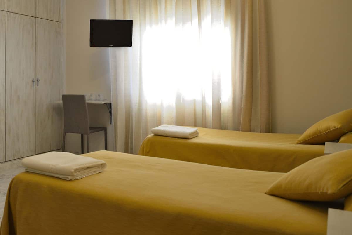 A hotel room with two beds, a desk, a chair, and a TV on the wall.