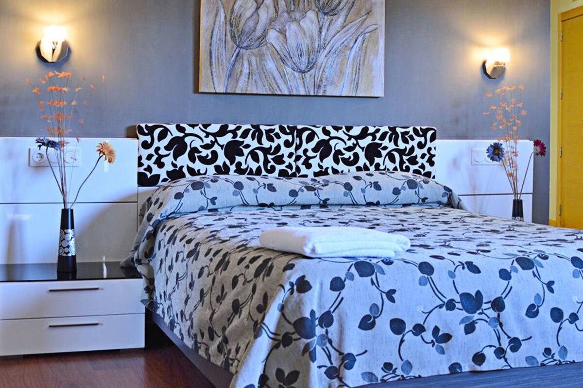 A bedroom with a bed, bedside tables, a nightstand, a wall-mounted artwork, and a door.
